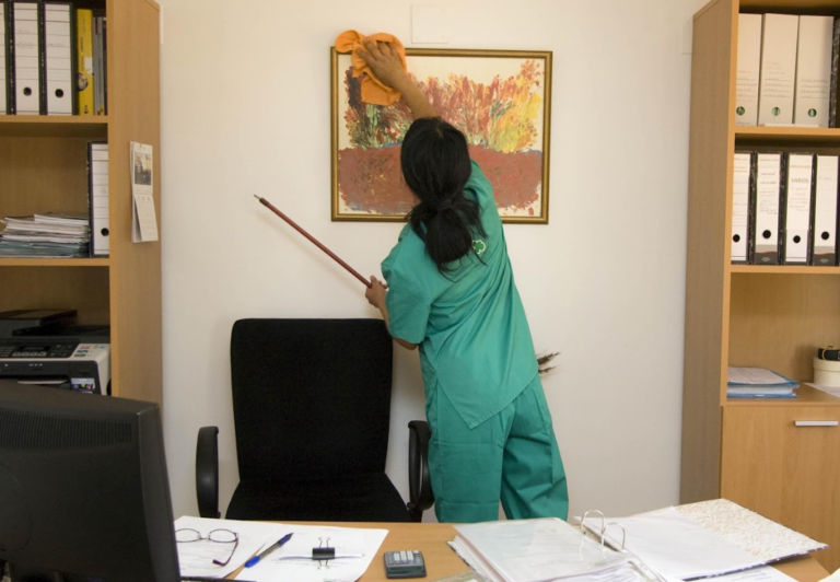 Rengørings assistent der foretager sig privat rengøring på kontor. iført rengøringstøj.