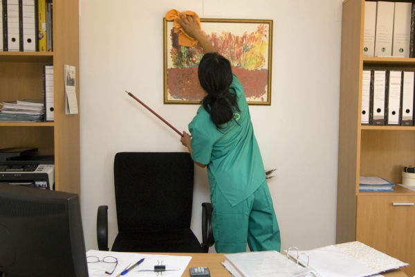 Rengørings assistent der foretager sig privat rengøring på kontor. iført rengøringstøj.